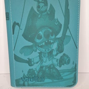 Puede incluir: Carpeta de tarjetas de color turquesa con una ilustración de un personaje de dibujos animados con temática pirata, con un sombrero y sosteniendo una espada y un cañón. La palabra "vaultx" está impresa en la parte inferior. La carpeta tiene un borde cosido y el texto "TEAR" en el lateral.