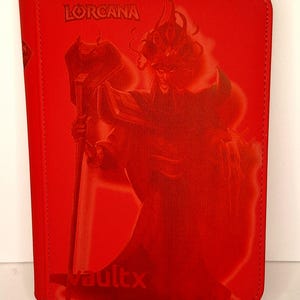 Puede incluir: Funda roja para tarjetas con la palabra "LORCANA" en la parte superior y "vaultx" en la inferior. Una ilustración roja de un personaje con un bastón en el centro. La funda es rectangular y tiene un borde cosido.