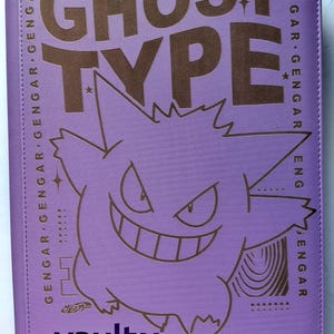 Puede incluir: Un archivador de cartas morado con un gráfico marrón del personaje Gengar y las palabras "GHOST TYPE". El archivador tiene el texto "CATEGORY: SHADOW POKEMON" y "GENGAR" impreso. La marca "vaultx" está impresa en la parte inferior.
