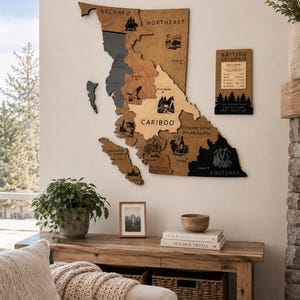 May include: A large wooden wall map of British Columbia featuring distinct regional sections in varying wood tones. The map includes engraved text labels for regions like Nechako, Cariboo, and Kootenay, along with small illustrative icons and a separate legend.