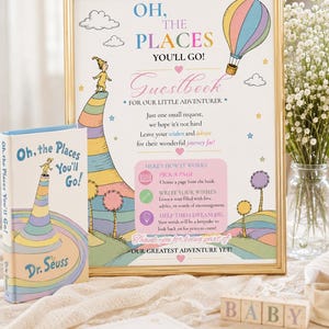 Peut inclure: Une affiche encadrée intitulée Oh, The Places You'll Go! Guestbook for our little adventurer, avec une montgolfière et des illustrations de paysage. À côté se trouvent un livre assorti, un bloc-notes, un stylo et des cubes en bois formant BABY.