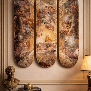 May include: Three skateboard decks with a classical painting design. The artwork features figures in a celestial scene with warm tones of brown, gold, and cream. The decks are mounted on a wall above a wooden table.