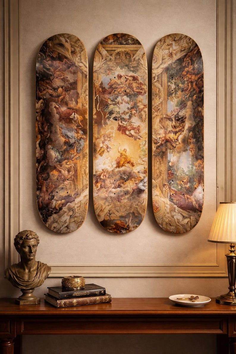 May include: Three skateboard decks with a classical painting design. The artwork features figures in a celestial scene with warm tones of brown, gold, and cream. The decks are mounted on a wall above a wooden table.