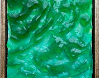 May include: Square abstract art piece with a textured, glossy, green surface, framed in a dark brown wooden frame. The artwork has a flowing, organic appearance, with varying shades of green creating depth and visual interest.