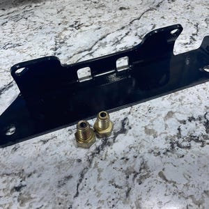 May include: A black metal bracket with multiple holes and a rectangular shape, accompanied by two brass fittings. The bracket has a glossy finish and appears to be a component of a larger mechanical assembly.