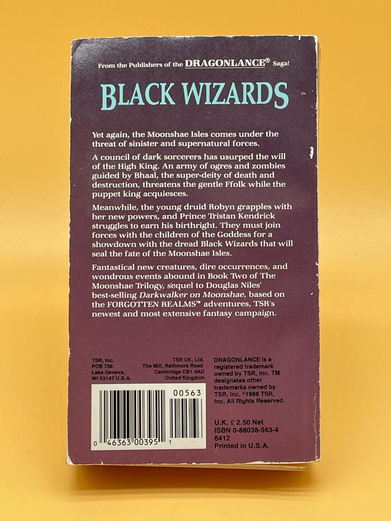 Op de afbeelding: Een vintage paperback boek getiteld "Black Wizards" uit de Dragonlance Saga. De omslag is donker met witte en blauwgroene tekst. De achterkant van het boek bevat een samenvatting van het fantasieverhaal en auteurinformatie.