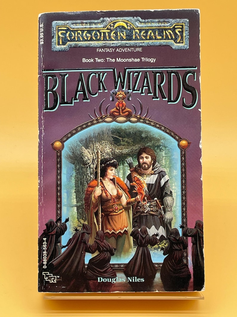 Op de afbeelding: Een paperback boek getiteld "Black Wizards" uit de Forgotten Realms-serie. De cover toont fantasy-kunst met twee figuren, een vrouw en een man, en verschillende figuren met capuchons. Het boek is Boek Twee van The Moonshae Trilogy.