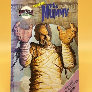 May include: A vintage book cover for "The Mummy" from Universal Monsters. The cover shows an illustration of the Mummy with outstretched arms. The title is in blue, and the book has a pink and purple border with text that reads "Full-Colour Pull-Out Poster Inside!"