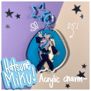 Könnte beinhalten: Ein Hatsune Miku Acryl-Anhänger, ca. 6,35 cm hoch, mit einer Cartoon-Figur mit langen türkisfarbenen Zöpfen. Der Anhänger hat einen sternförmigen Verschluss und den Text "Hatsune Miku! Acrylic charm~" in blauer Schrift.