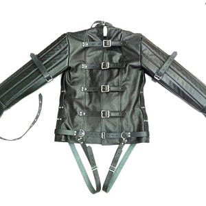 Puede incluir: Chaqueta de cuero negro con múltiples correas y hebillas. La chaqueta tiene mangas largas y cuello alto. Las mangas están acolchadas y tienen correas adicionales. La chaqueta está diseñada con múltiples correas y hebillas metálicas.