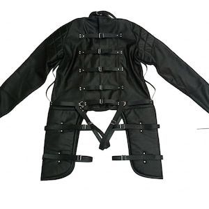 May include: Black garment with long sleeves and multiple straps. The garment has a quilted pattern on the shoulders and features several buckles and straps. The design includes attached leg coverings with additional straps and buckles.