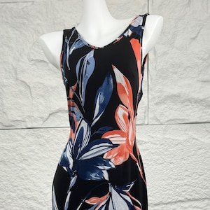 Op de afbeelding: Zwarte mouwloze jurk met een bloemenpatroon. De jurk heeft een V-hals en een getailleerd silhouet. Het bloemmotief bevat blauwe, witte en oranje bladachtige vormen. De jurk wordt gepresenteerd op een mannequin.