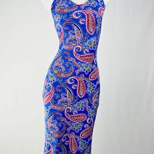 Könnte beinhalten: Ein ärmelloses Neckholder-Kleid mit einer leuchtend blauen Grundfarbe und einem komplizierten, mehrfarbigen Paisley-Muster in Rosa-, Weiß- und Hellblautönen. Das Kleidungsstück hat eine körperbetonte Silhouette, die bis zur Wadenmitte reicht.