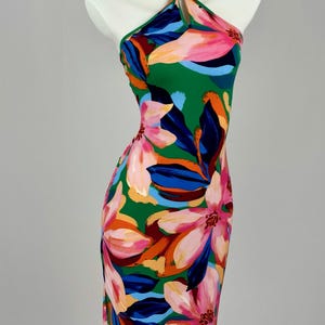 Könnte beinhalten: Grünes Neckholder-Kleid mit einem lebendigen Blumenmuster. Das Kleid hat große rosa, orange und blaue Blumen auf grünem Hintergrund. Das Kleid wird auf einer Schaufensterpuppe präsentiert.