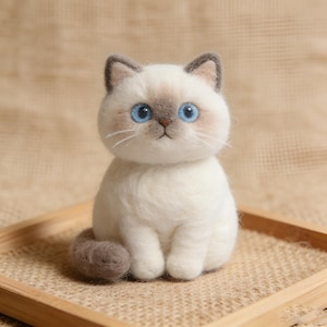 Peut inclure: Figurine de chat blanc faite à la main, avec des yeux bleus et des détails gris. Le chat est assis sur un plateau en bois. Le chat a des oreilles grises et une queue grise. Le chat a une expression douce.