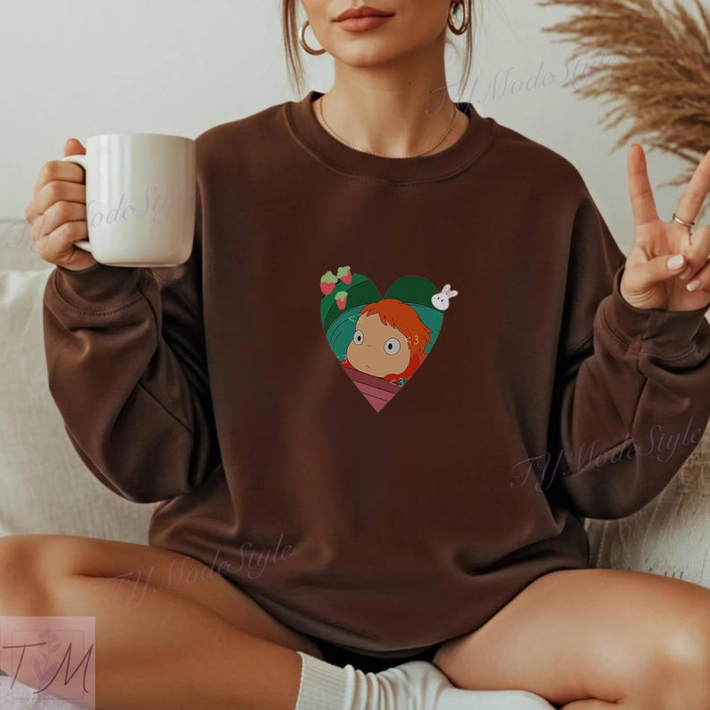 May include: A brown sweatshirt featuring a heart-shaped graphic with a cartoon girl with red hair, a white rabbit, and strawberries. The sweatshirt is a solid brown color.