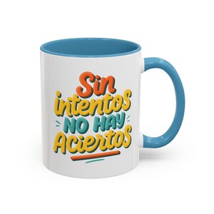 May include: White ceramic mug with a blue interior and handle. The mug features the Spanish phrase "Sin intentos NO HAY Aciertos" in orange, yellow, and blue lettering. A colorful and motivational coffee mug.