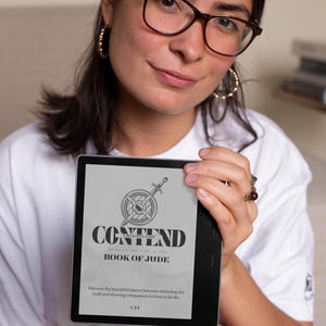 Może przedstawiać: Czytnik e-booków wyświetla tytuł "CONTEND" z podtytułem "BOOK OF JUDE" oraz grafiką miecza i tarczy. Poniższy tekst brzmi: "Odkryj piękną równowagę między obroną prawdy a okazywaniem współczucia tym, którzy wątpią."