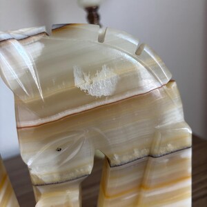 May include: Close-up of a carved onyx horse head sculpture. The sculpture features a cream, brown, and yellow color palette with visible veining. The horse head has a detailed mane and is part of a decorative art piece.