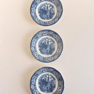 May include: Three round ceramic plates arranged vertically, each featuring a blue and white transferware pattern. The center of each plate depicts a church building with a tall steeple, surrounded by a wide border of detailed floral motifs.