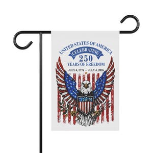 Puede incluir: Una bandera de jardín blanca con un soporte de metal negro. La bandera presenta un diseño patriótico con un águila, la bandera estadounidense y el texto "UNITED STATES OF AMERICA CELEBRATING 250 YEARS OF FREEDOM JULY 4, 1776 - JULY 4, 2026."
