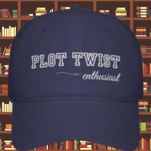 Puede incluir: Gorra de béisbol azul marino con las palabras "PLOT TWIST" en blanco, letras delineadas. Debajo, una línea curva y la palabra "enthusiast" en cursiva. La gorra tiene una visera curva y una corona estructurada.
