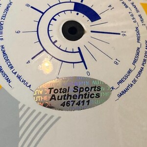 Puede incluir: Una superficie circular blanca con un gr&aacute;fico de man&oacute;metro azul con marcas de 0 a 18 PSI. Una pegatina hologr&aacute;fica ovalada est&aacute; centrada en la superficie, mostrando el texto Total Sports Authentics y el n&uacute;mero 467411 en negro.