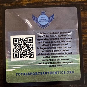 May include: A square authentication card with a QR code and the Total Sports Authentics logo. The card has text stating the item has been examined and is deemed genuine. The website address is also visible.
