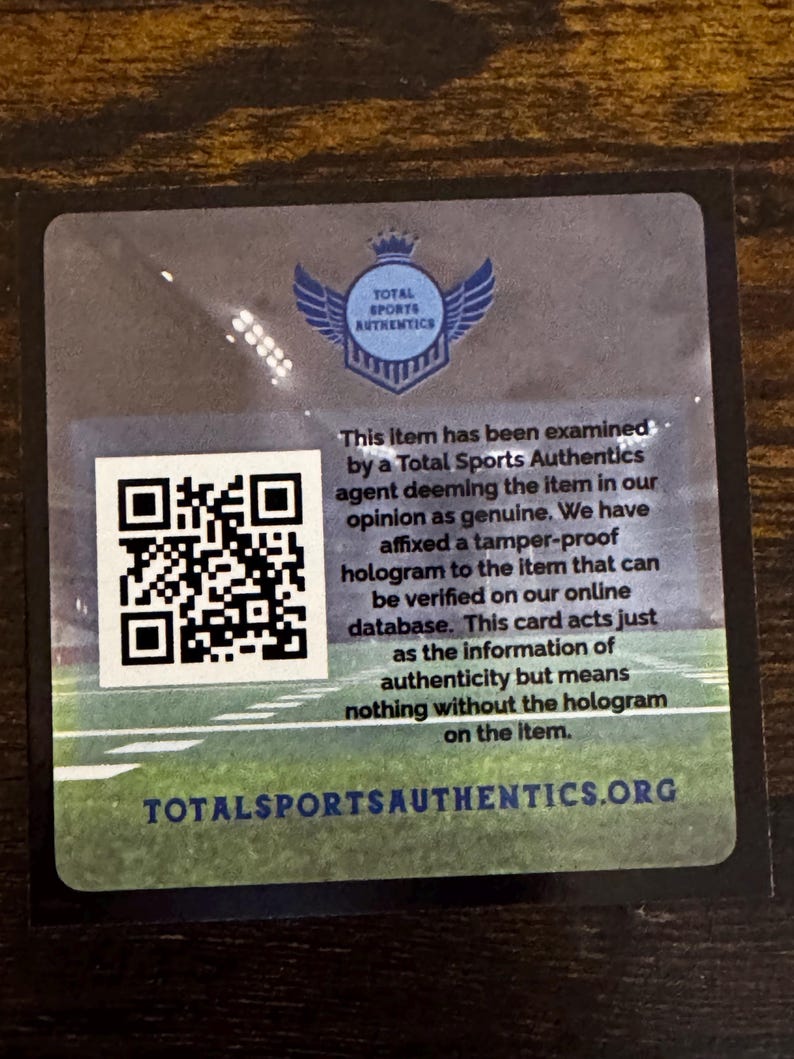 May include: A square authentication card with a QR code and the Total Sports Authentics logo. The card has text stating the item has been examined and is deemed genuine. The website address is also visible.