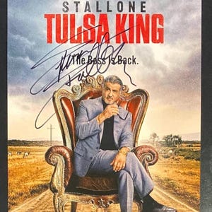 May include: A promotional poster for Tulsa King featuring Sylvester Stallone sitting in a large ornate leather chair. The text reads STALLONE TULSA KING, The Boss Is Back, and NEW SEASON. A black ink autograph is written across the center.