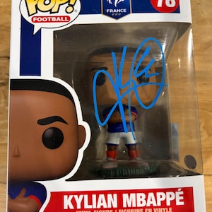 以下が含まれることがあります： フランス代表のロゴが入ったFunko Pop Footballのキリアン・エムバペのビニール製フィギュア（番号78）です。オリジナルの箱に入っており、透明なプラスチック窓には青いインクでサインが書かれています。フィギュアは青いユニフォームと白いショートパンツを着用しています。