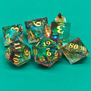 Könnte beinhalten: Sieben transparente, polyedrische Würfel mit goldenen Zahlen und Einschlüssen in Grün, Blau und Gold. Die Würfel liegen auf einer grünen Oberfläche, ideal für Rollenspiele.