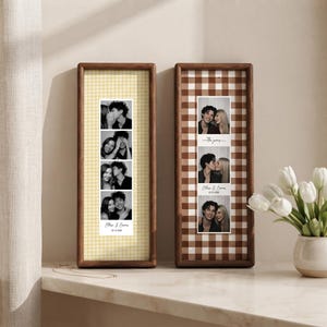 May include: Two vertical wooden frames containing photo strips. The left frame has a yellow gingham background with a black and white photo strip of a couple and the text Ethan & Emma 02.15.2026. The right frame has a brown gingham background.
