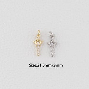 May include: Two decorative pendants, one gold-toned and one silver-toned, each featuring a crown and wing design with embedded clear crystals. The text "Size: 21.5mmx8mm" is displayed below the pendants.