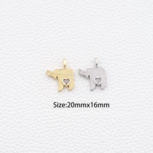 May include: Two small elephant pendants, one gold-toned and one silver-toned, each with a heart-shaped detail. The pendants are approximately 20mm x 16mm in size. The background is a textured, off-white surface.