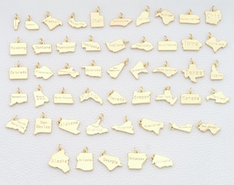 May include: A collection of gold-colored pendants, each shaped like a U.S. state. The names of the states are engraved on each pendant. The pendants are small, with a simple loop for attaching to a chain or bracelet.