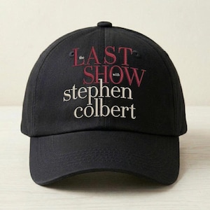 May include: Black baseball cap featuring the text "the LAST SHOW with stephen colbert" embroidered in white and maroon. The cap has a curved brim and a button on top. A stylish accessory for fans of the show.