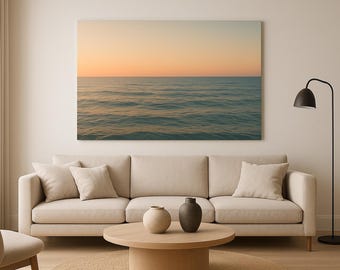 May include: A large canvas print of an ocean scene with a sunset sky hangs above a beige sofa. The room features a round wooden coffee table with two vases, a floor lamp, and a beige chair. The overall aesthetic is minimalist and calming.