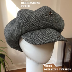 May include: A gray and black herringbone tweed newsboy cap with a large, rounded crown and a short brim. The cap has a button on the top and a metal pin on the side. The text "NIKKI OVERSIZED NEWSBOY BIG VERSION" is printed on the bottom of the image.