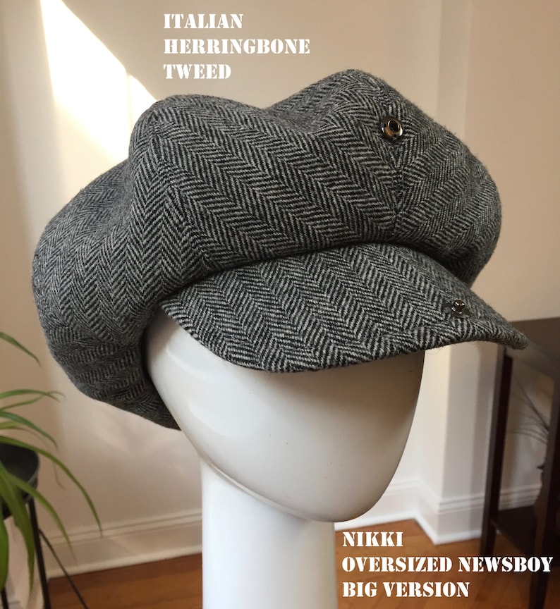 May include: A gray and black herringbone tweed newsboy cap with a large, rounded crown and a short brim. The cap has a button on the top and a metal pin on the side. The text "NIKKI OVERSIZED NEWSBOY BIG VERSION" is printed on the bottom of the image.