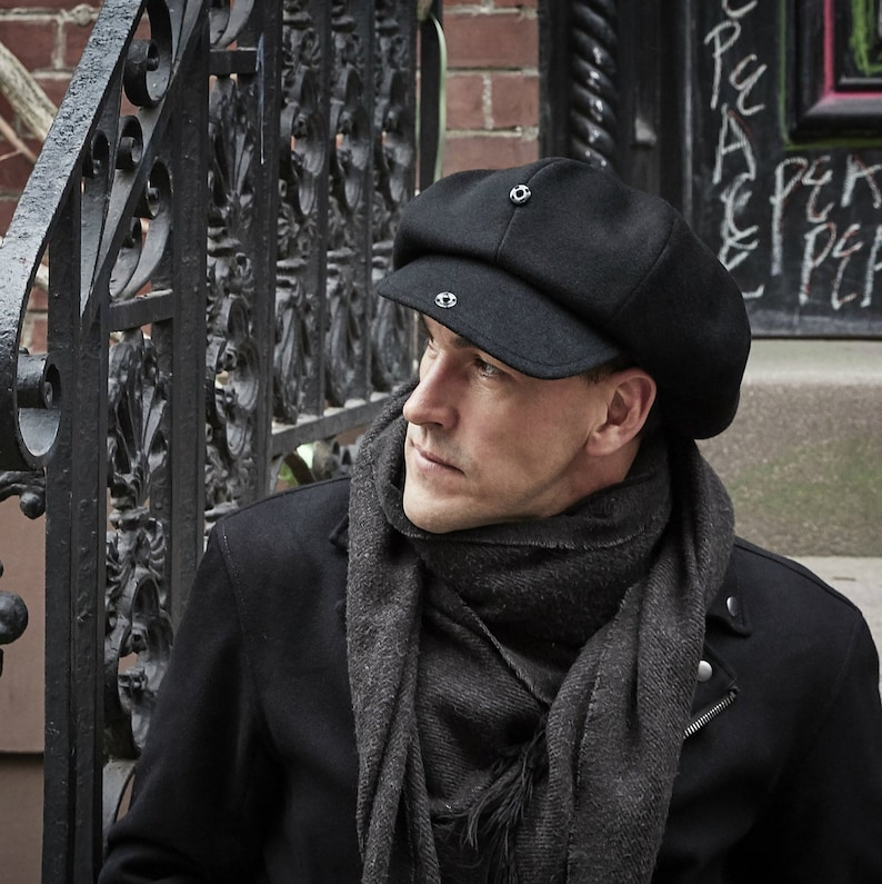 May include: A man wearing a black newsboy cap with a gray scarf. The cap has two silver buttons on the front.