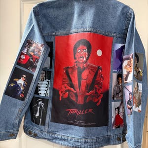 May include: Light blue denim jacket featuring a large red graphic of Michael Jackson from the "Thriller" music video on the back. Additional images of Michael Jackson are printed on the sleeves and back. The jacket has a button-up front and a collared neckline.