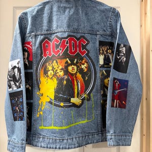 May include: A light blue denim jacket with AC/DC band graphics. The back features a large image of the band with the words "Highway to Hell". Several smaller patches with band imagery are also visible on the jacket.