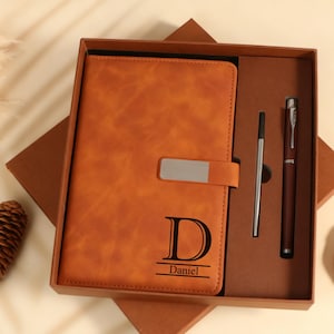 Op de afbeelding: Een cadeau set met een bruin leren notitieboek met een zilveren sluiting, een pen en een balpen. Het notitieboek is voorzien van de letter "D" en de naam "Daniel".