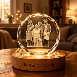 May include: A crystal photo sphere displaying a family portrait, lit from within. The sphere rests on a wooden base inscribed with "Heart of Our Family." Decorative crystal pieces are scattered around the base.
