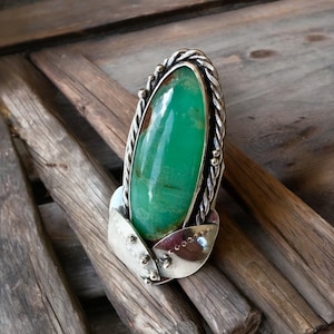 May include: A silver ring featuring a large green gemstone set in a twisted silver band. The ring is embellished with small silver beads.