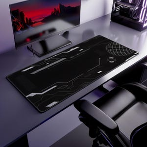 May include: A black gaming mouse mat with a white geometric design and a grid pattern. The mat is rectangular and sits on a desk with a computer monitor and a gaming chair in the background.