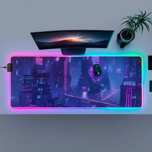 Peut inclure: Tapis de souris de jeu rectangulaire avec un design de paysage urbain futuriste dans les tons de violet, bleu et rose. Le tapis a un bord lumineux à LED. Une souris noire et un écran d'ordinateur sont dessus.