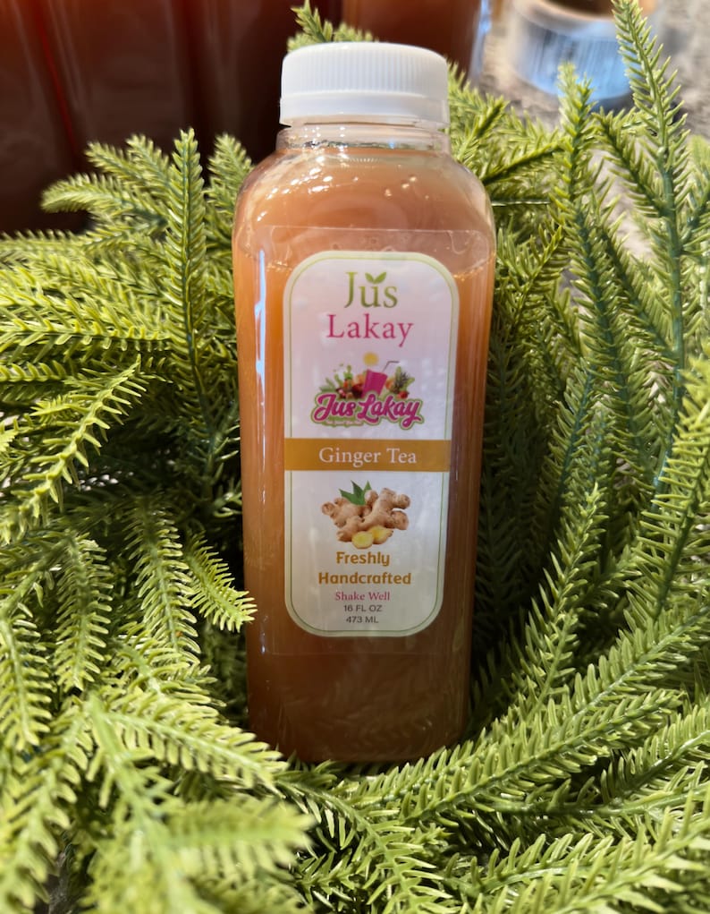 Peut inclure: Une bouteille en plastique transparente remplie de th&eacute; au gingembre, &eacute;tiquet&eacute;e "Jus Lakay". L'&eacute;tiquette indique "Ginger Tea" et "Freshly Handcrafted". La bouteille est entour&eacute;e de feuillage vert. Contient 473 ml de th&eacute;.