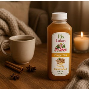 May include: A bottle of Jus Lakay Ginger Tea with a white cap, next to a mug of tea, cinnamon sticks, star anise, and a lit candle. The label reads "Freshly Handcrafted" and the bottle contains 16 fl oz (475 ml) of tea.